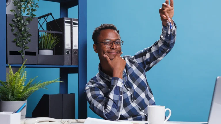 Smiling young entrepreneur holding house keys while sitting at office desk