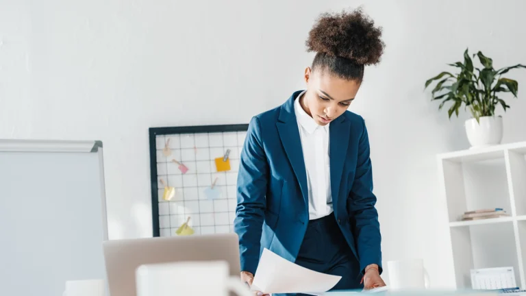 African businesswoman in blue suit analyzing documents at desk in a bright modern office.