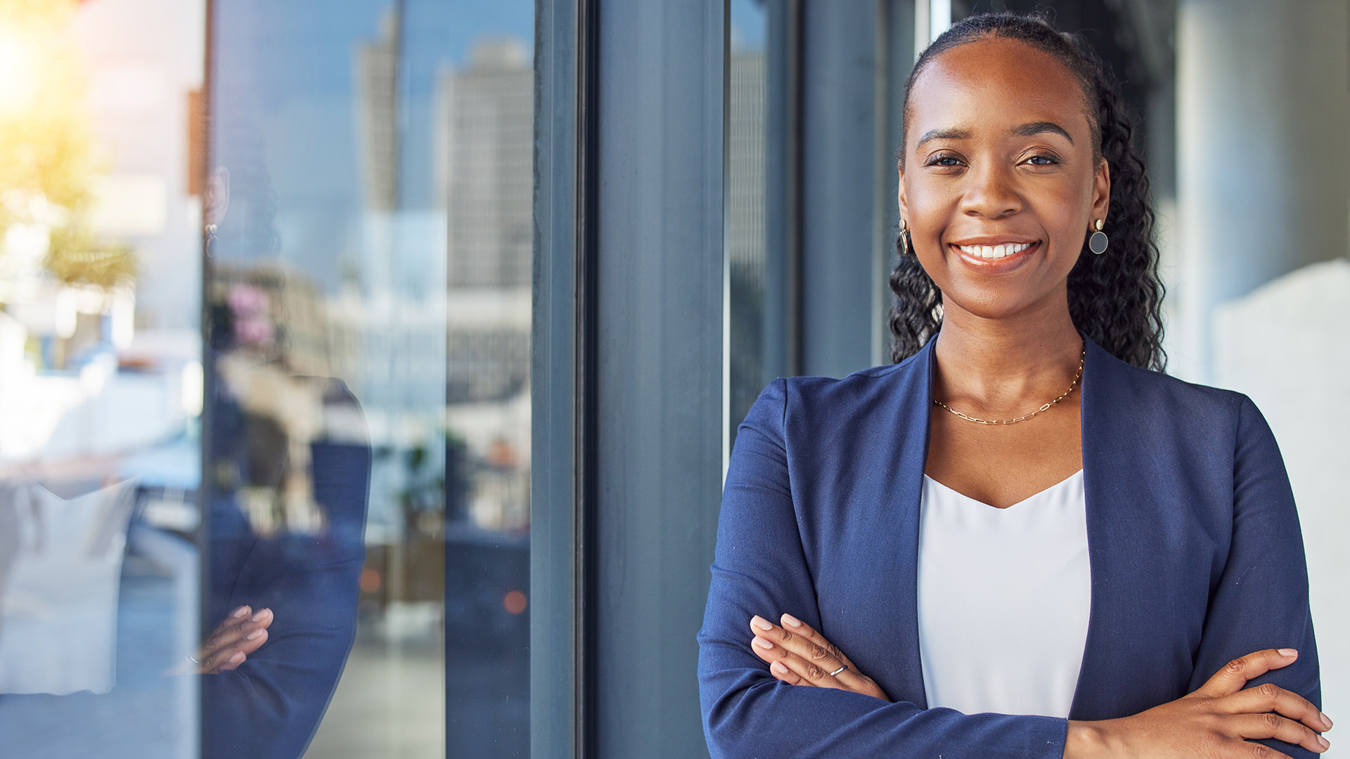 Confident young black woman in business attire standing with arms crossed outside a modern office building