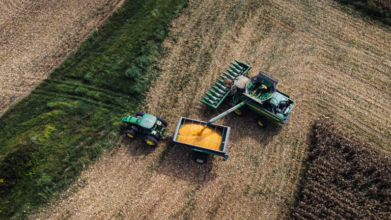 Aerial view of combine harvester unloading corn into a tractor trailer on a farm field