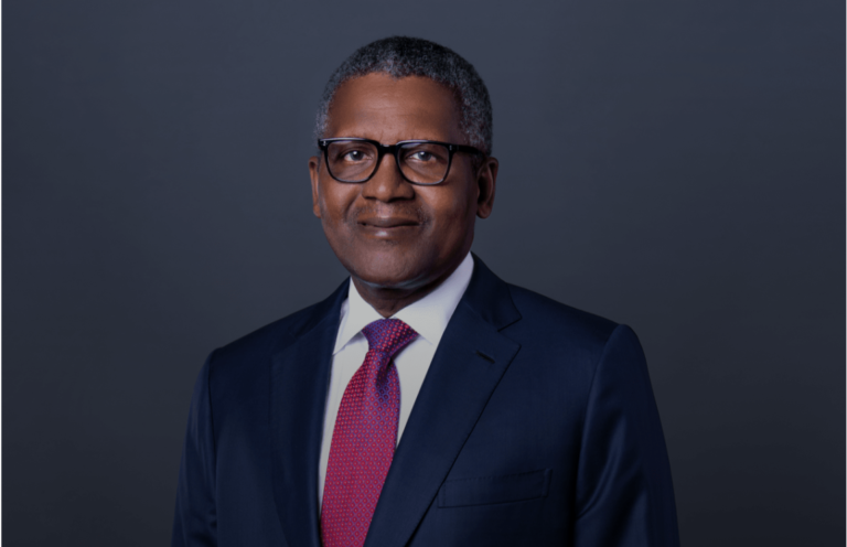 Aliko Dangote, wearing glasses and a suit with a red tie, smiling confidently in a formal portrait.