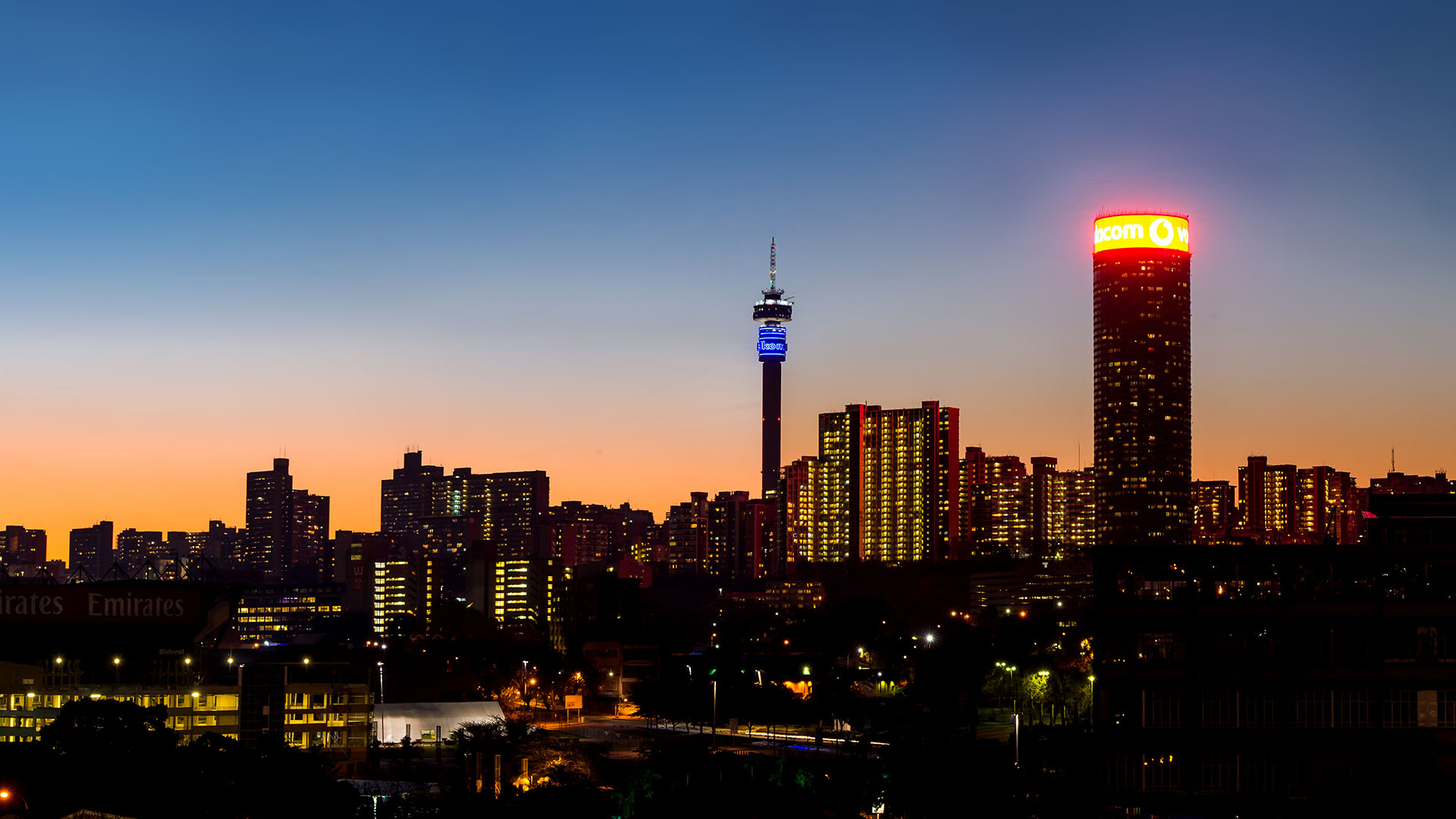 A stunning view of the johannesburg skyline at dusk featuring the iconic hillbrow tower and illuminated buildings against a vibrant sunset backdrop