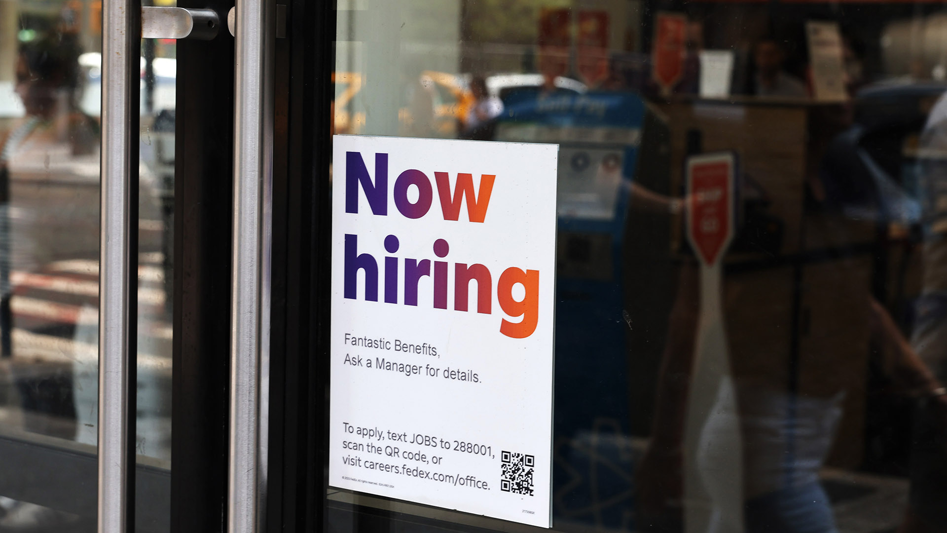 Job Market Surge: Now Hiring Sign in Storefront | Brimco A now hiring sign posted on the glass door of a store offering details on job benefits and application instructions