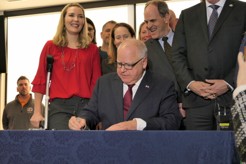 Gov Tim walz signing a bill into law at the st Paul labor center surrounded by supporters