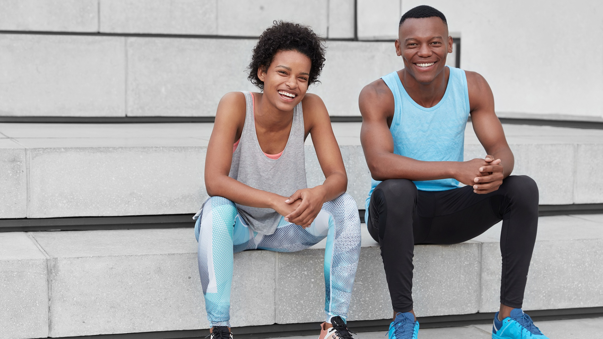 Young african man and woman sitting on outdoor concrete steps in athletic wear smiling after a workout