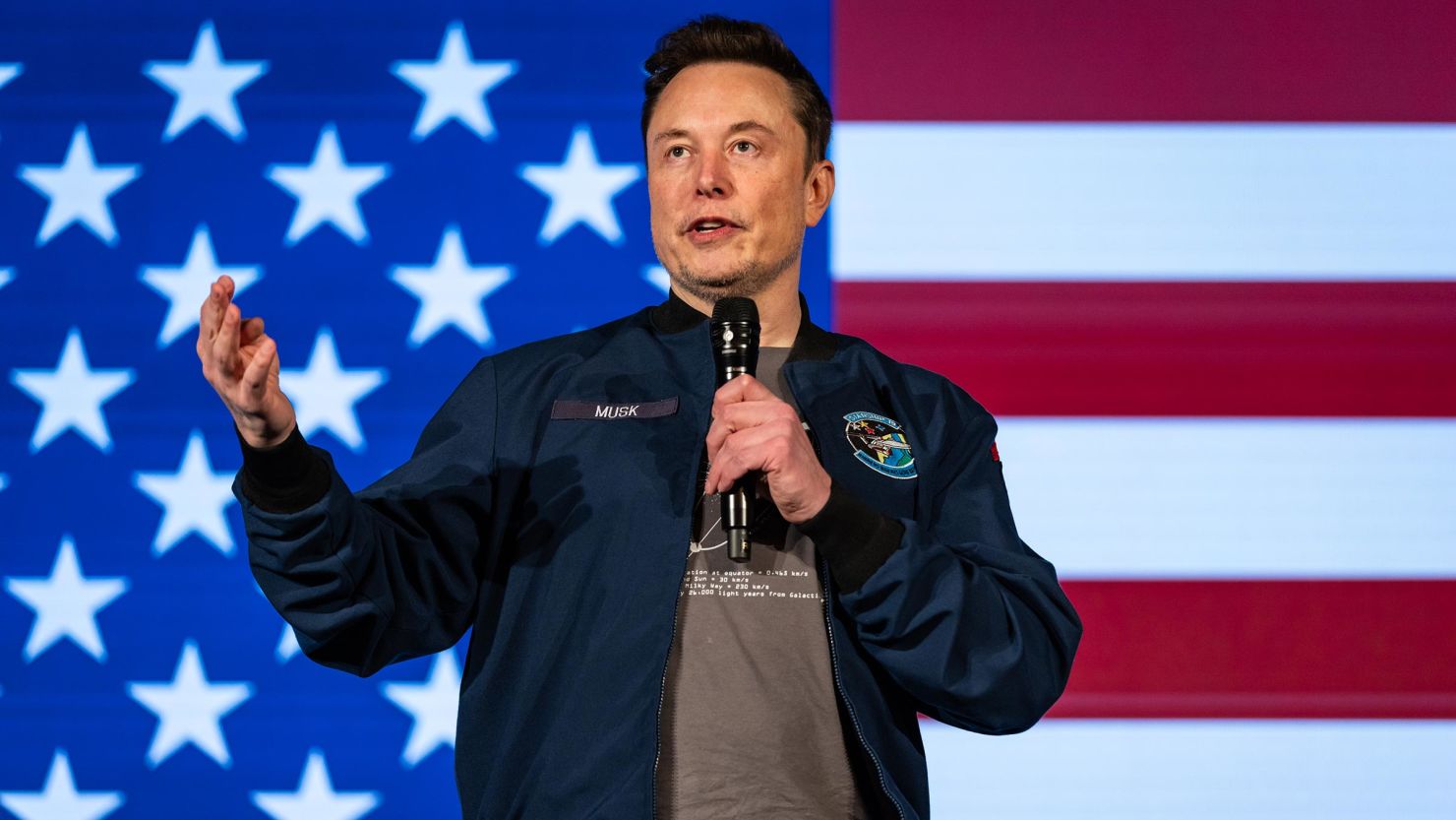 Elon Musk Addresses the Crowd with Vision for Americas Future | Brimco Elon musk holding a microphone and speaking in front of an american flag backdrop