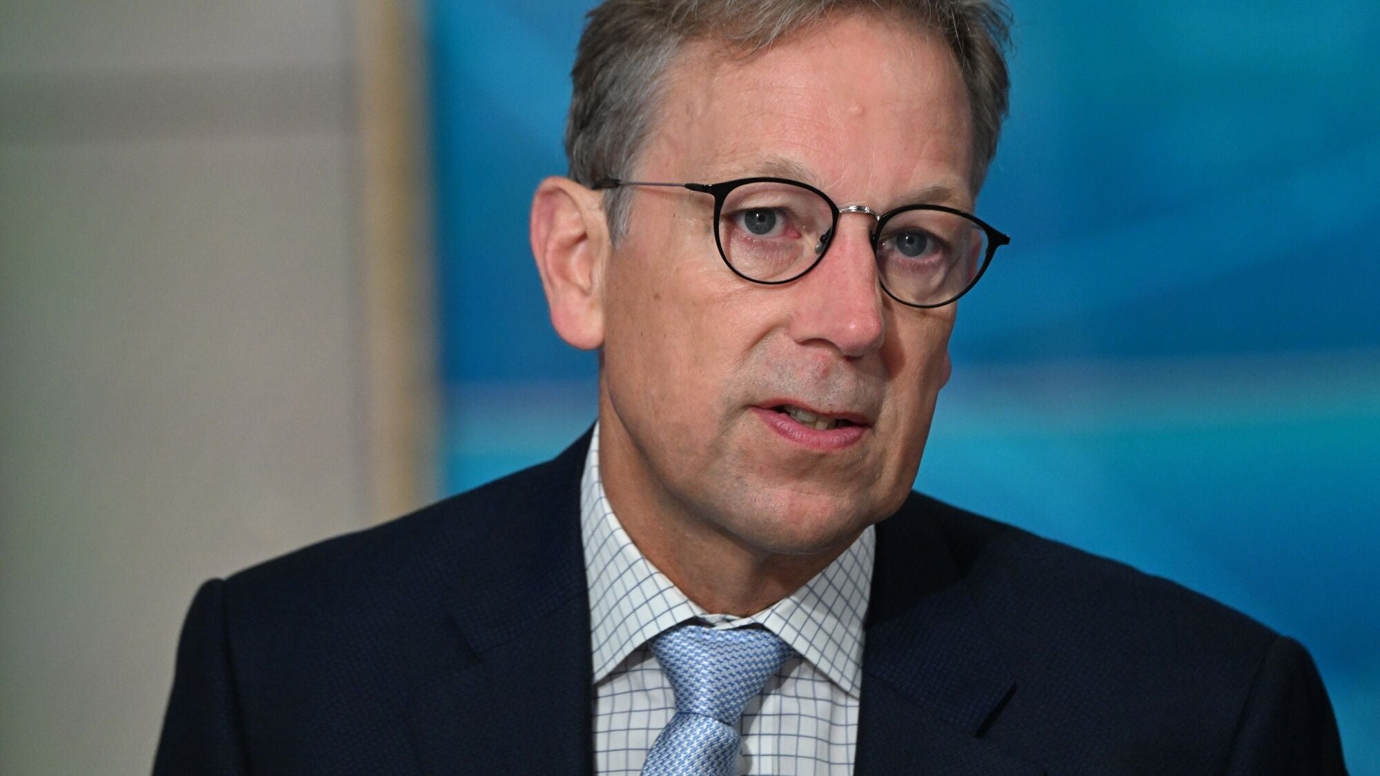 Jakob Stausholm Discusses Global Mining and Sustainability Initiatives | Brimco Jakob stausholm ceo of rio tinto wearing glasses a dark suit and a patterned tie speaking during an interview with a blue background