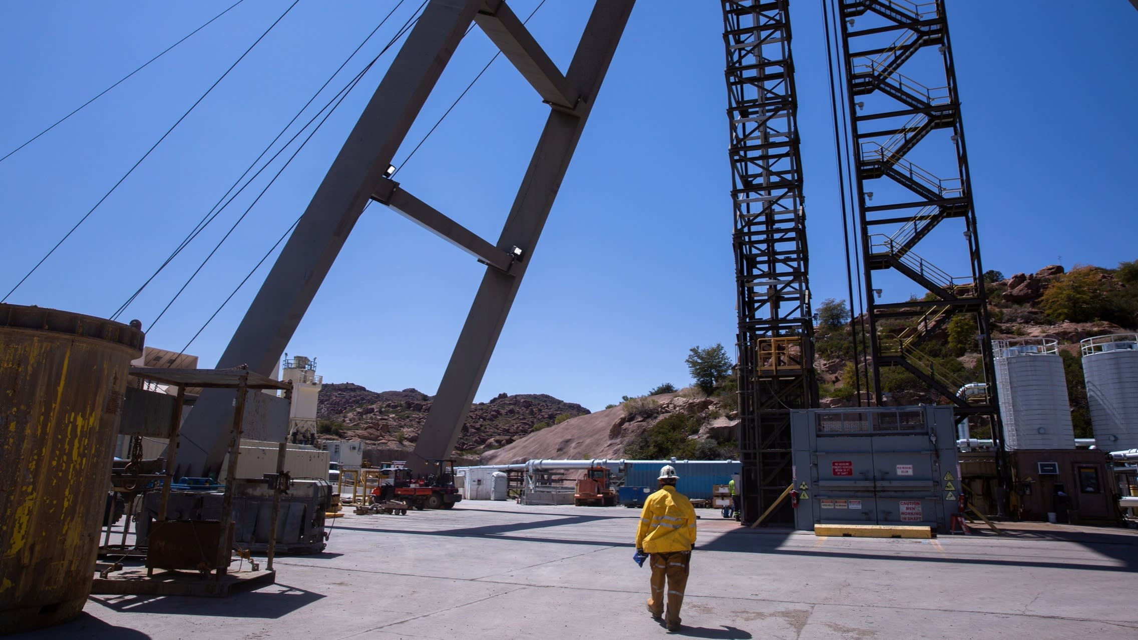 rio-tinto-bets-trump-will-give-green-light-to-us-copper-mine | Brimco A worker in a yellow safety jacket walks through a copper mining site with large industrial structures cables and equipment against a desert like landscape