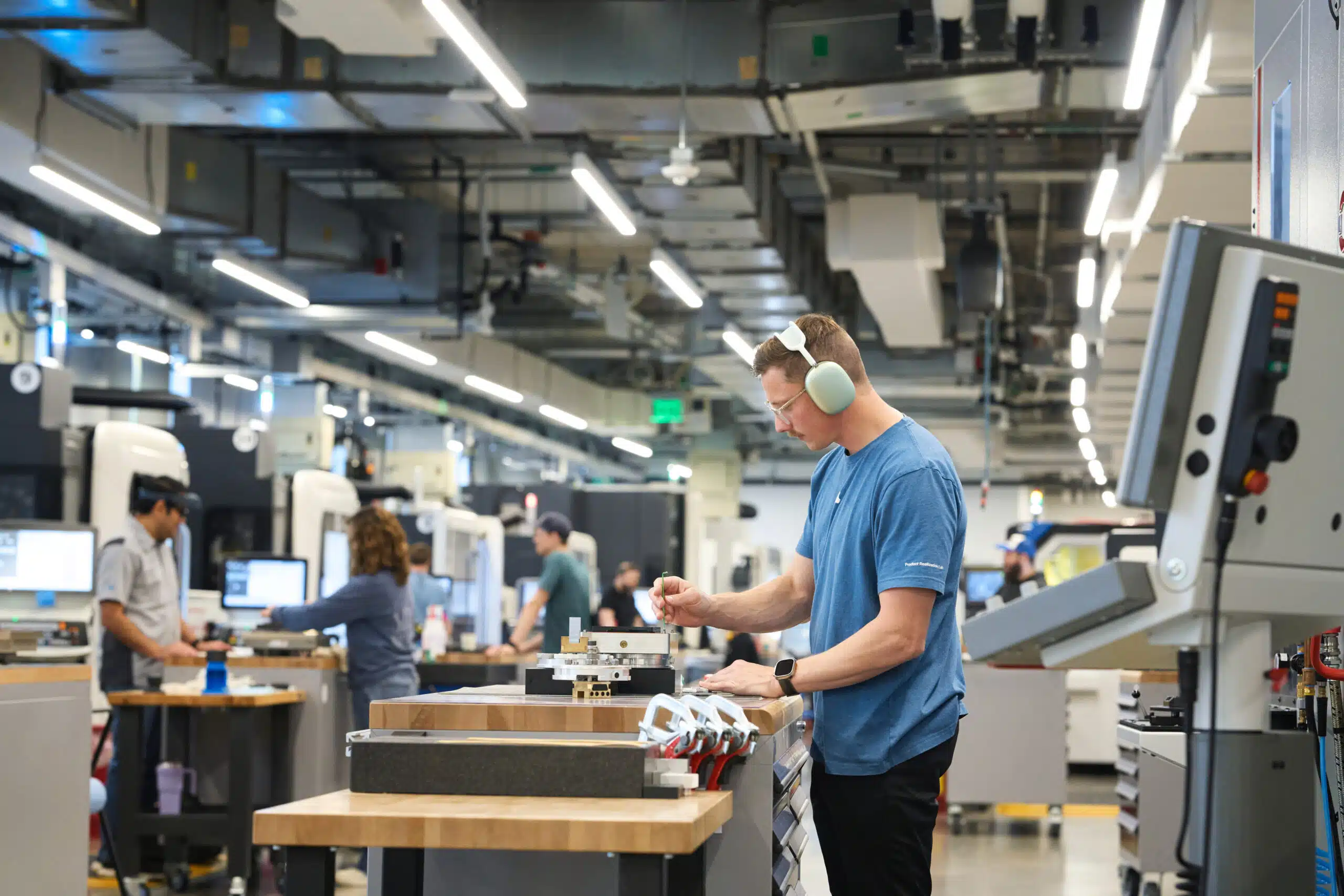 Apple-US-investment-Austin-research-facility-01 | Brimco Apple technician wearing hearing protection works inside a high tech research and manufacturing facility with colleagues in the background
