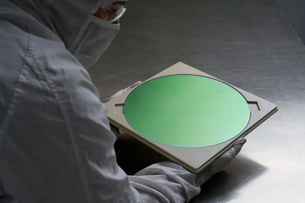 Apple-US-investment-semiconductor-wafer | Brimco A cleanroom technician in protective gear inspecting a green semiconductor wafer on a tray