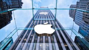 Looking up at apples glass storefront on fifth avenue with the apple logo and skyscrapers reflecting in the glass