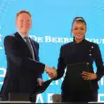 De beers ceo and bogolo kenewendo shaking hands after signing the de beers   botswana partnership agreement standing in front of a backdrop featuring the republic of botswana and de beers group logos