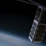 A eurosat satellite with extended solar panels floating above earth in space with the planets horizon visible in the background