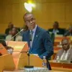 Ndaba Gaolathe, dressed in a navy-blue suit and tie, speaks at a podium in Parliament while delivering Botswana’s 2025/26 Budget Speech, with government officials seated in the background.