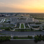 Aerial shot of the pentagon building at sunset showing its fivesided shape adjacent highways parking areas and the potomac river at the bottom of the frame