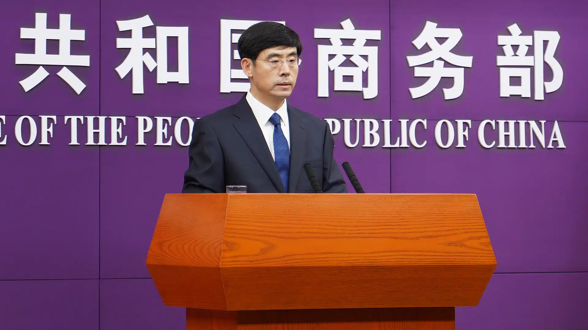 Chinese Commerce Ministry Spokesperson Delivers Official Statement | Brimco Chinese government spokesperson in a suit speaks at a podium in front of the ministry of commerce of china signage