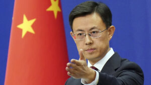 Guo jiakun chinese foreign ministry spokesperson in a dark suit and red tie gesturing with his hand while speaking in front of a blue backdrop and the chinese national flag