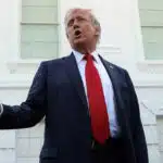 Donald trump speaking outside the white house in a navy blue suit and red tie mid gesture