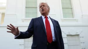 Donald trump speaking outside the white house in a navy blue suit and red tie mid gesture