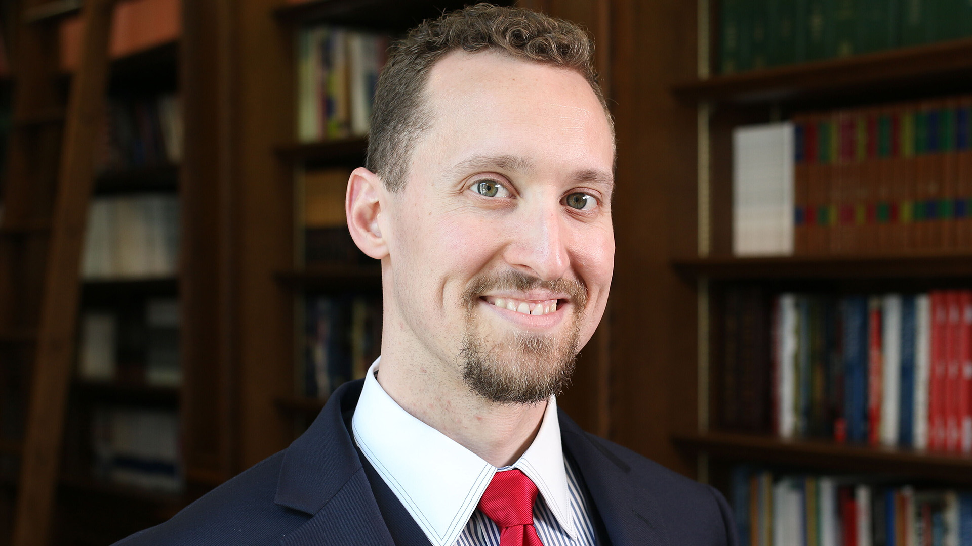 E.J. Antoni – Championing Fiscal Responsibility and Free Markets | Brimco E J Antoni smiling in a suit and red tie standing in front of bookshelves filled with academic texts