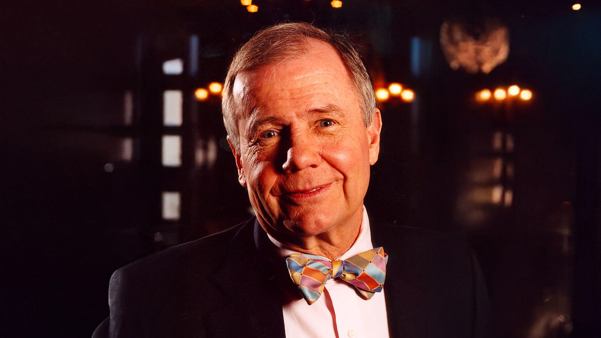 Jim rogers smiling in a bow tie and suit set against a warmly lit background