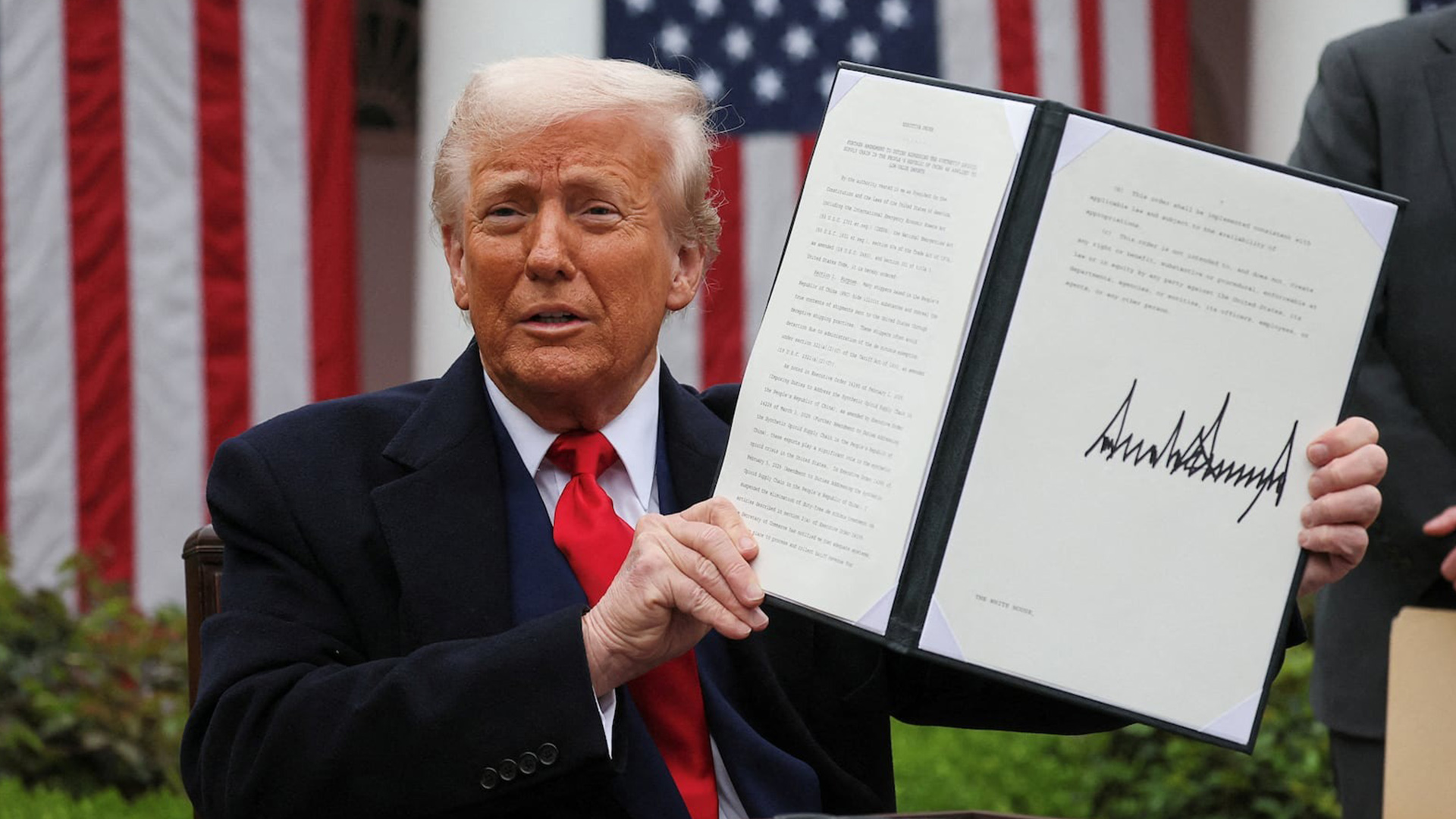 President Trump Signs Executive Order in White House Rose Garden | Brimco President donald trump holding up a signed executive order in the white house rose garden with american flags behind him