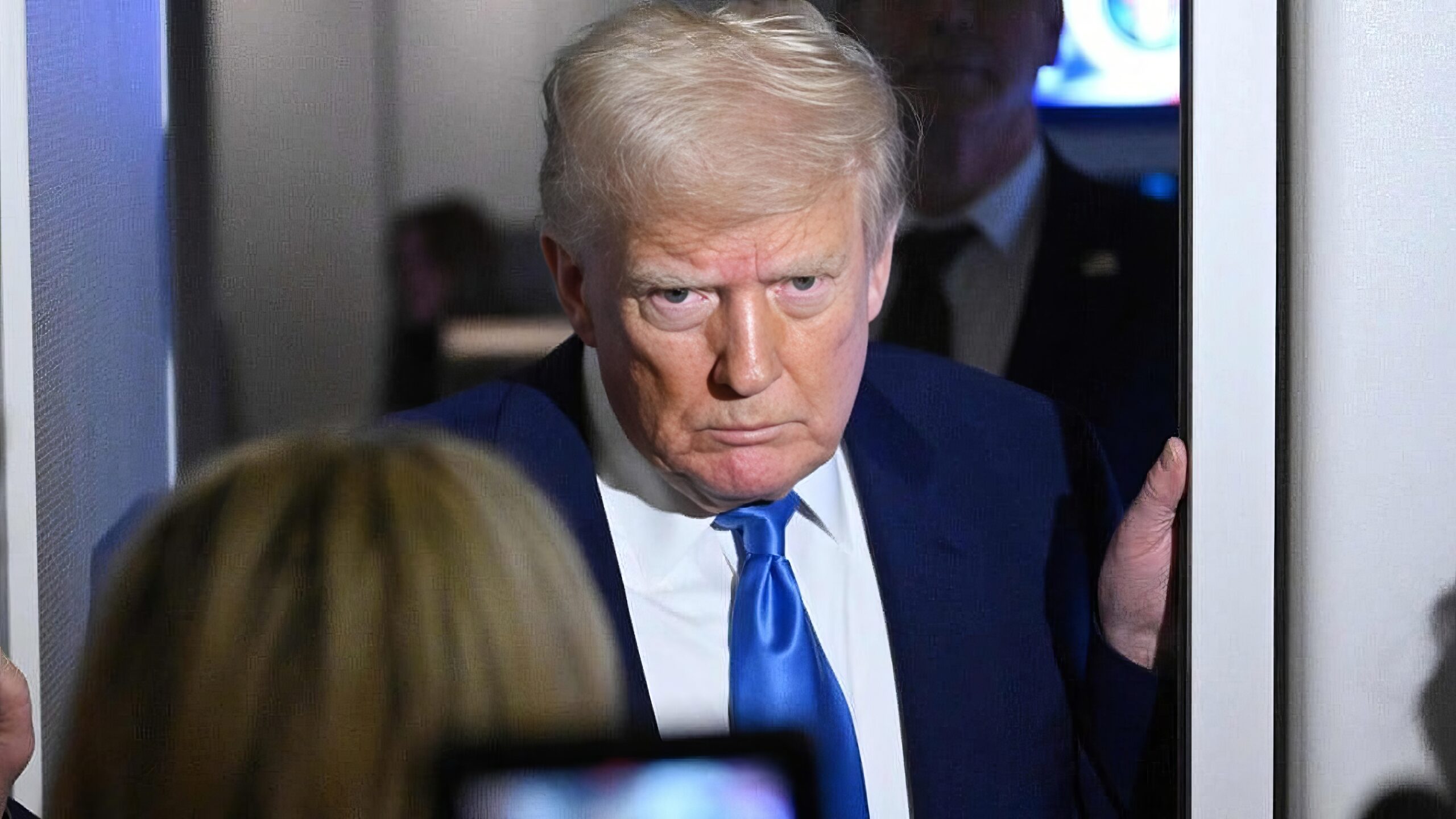 President Trump Takes Questions Aboard Air Force One-topaz | Brimco Donald trump aboard air force one leaning through a doorway speaking to reporters with a focused expression and a bright blue tie
