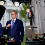 Scott bessent in a dark suit and green striped tie stands before cameras outside the treasury speaking and gesturing with his hands