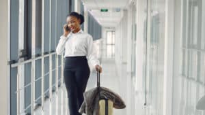 Professional woman on a secondment assignment walking through an airport with luggage while on a phone call
