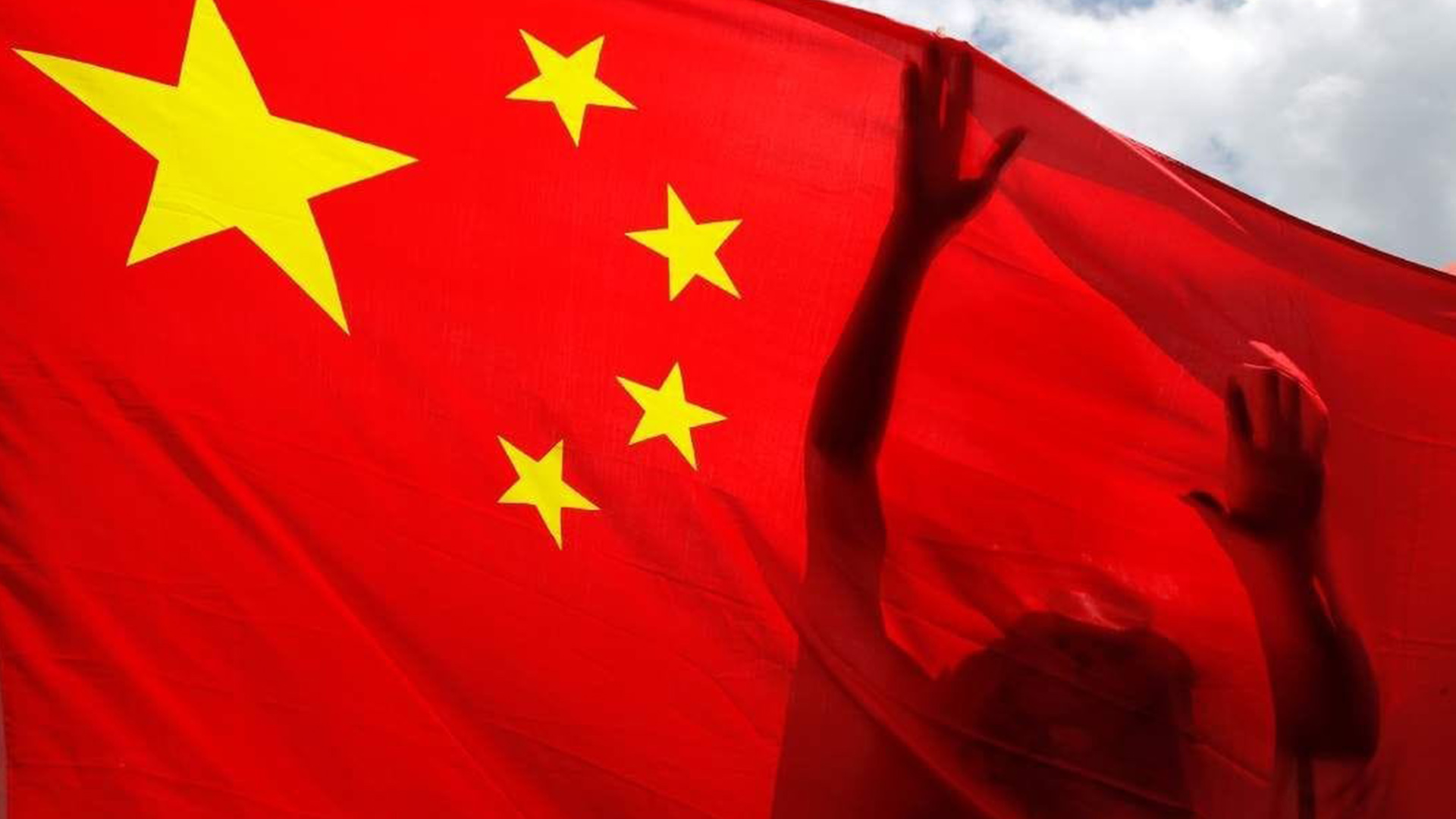 Shadowed Hands Behind the Chinese Flag | Brimco Silhouette of hands reaching up behind a translucent chinese flag fluttering against a partly cloudy sky