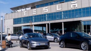 Tesla electric vehicles parked outside a tesla gigafactory with people walking and interacting near the cars