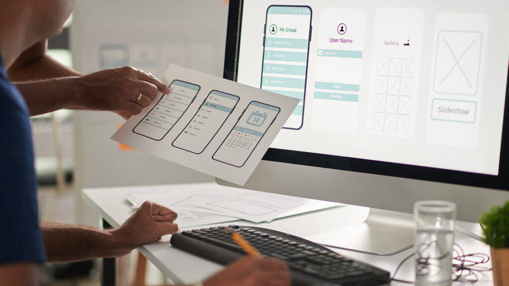 UX designers reviewing mobile interface prototypes and website feature layouts on a computer screen