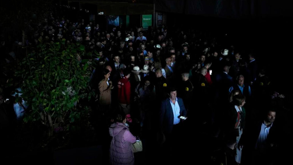 Large crowd standing in a dark venue using phone flashlights during a power outage