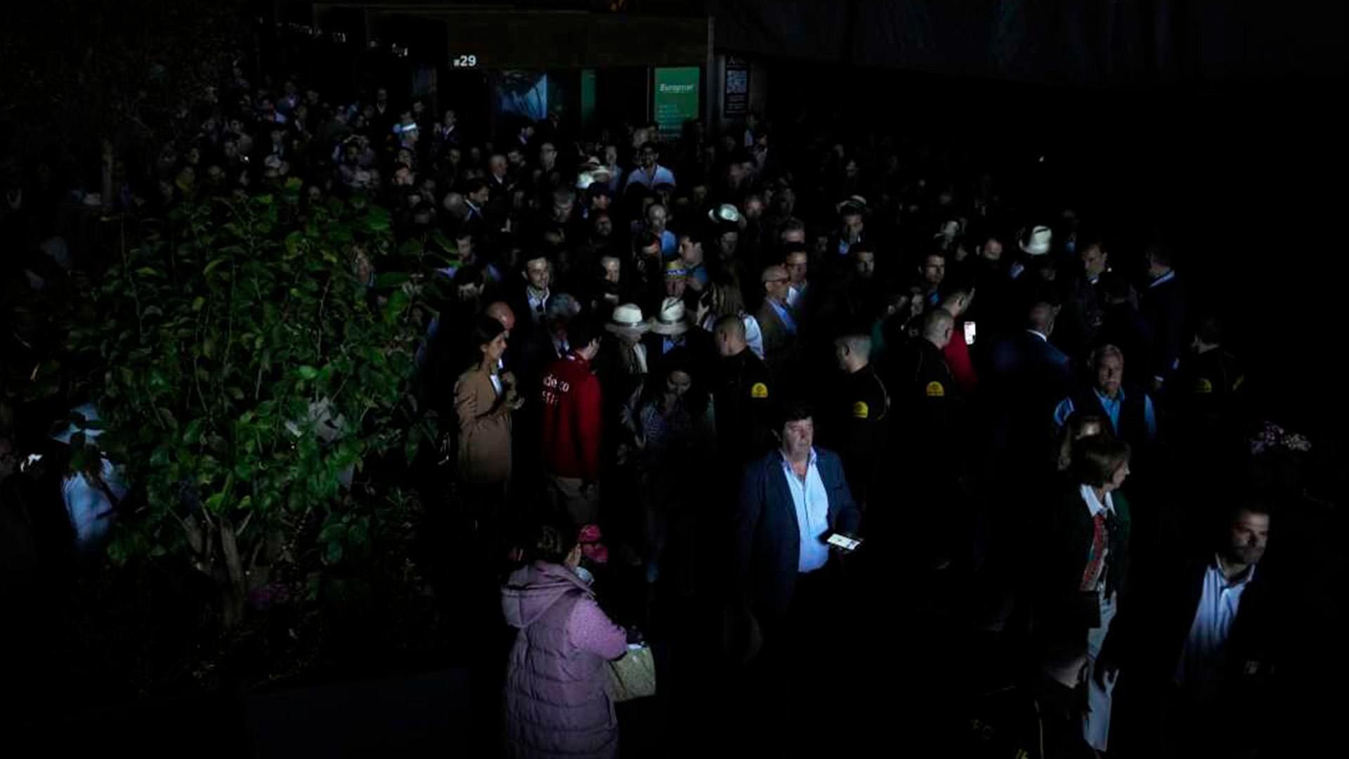 Crowd Gathers in Darkness Amid Power Outage_ | Brimco Large crowd standing in a dark venue using phone flashlights during a power outage