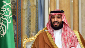 Crown prince mohammed bin salman in traditional saudi attire seated on a gilded chair with the saudi flag in the background