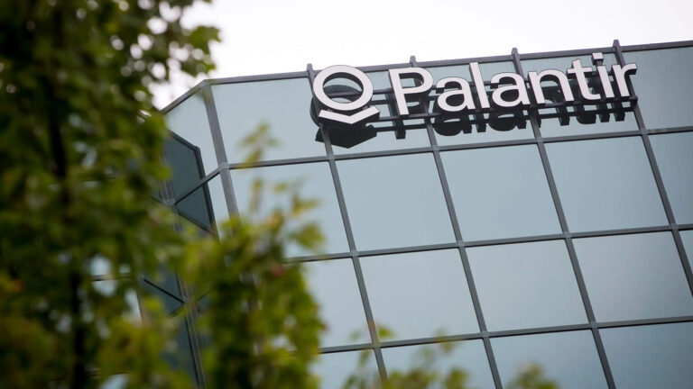 Glass-fronted building with the Palantir Technologies logo, partially obscured by green foliage.