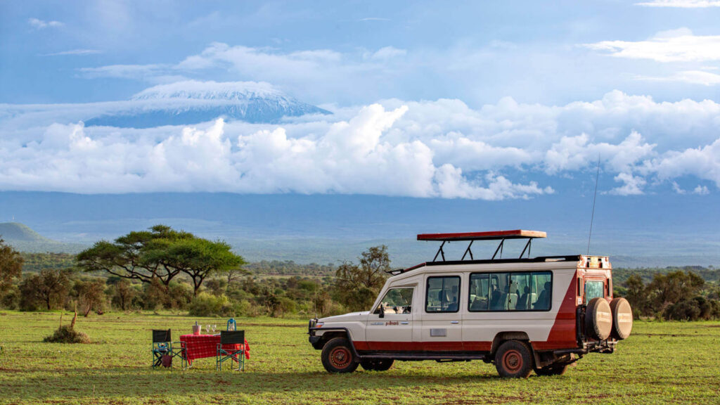 Pollmans tours safari vehicle and dining setup in grassy plains with mount kilimanjaro and clouds in the background