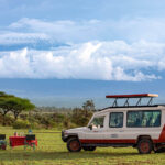Pollmans tours safari vehicle and dining setup in grassy plains with mount kilimanjaro and clouds in the background