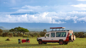 Pollmans tours safari vehicle and dining setup in grassy plains with mount kilimanjaro and clouds in the background
