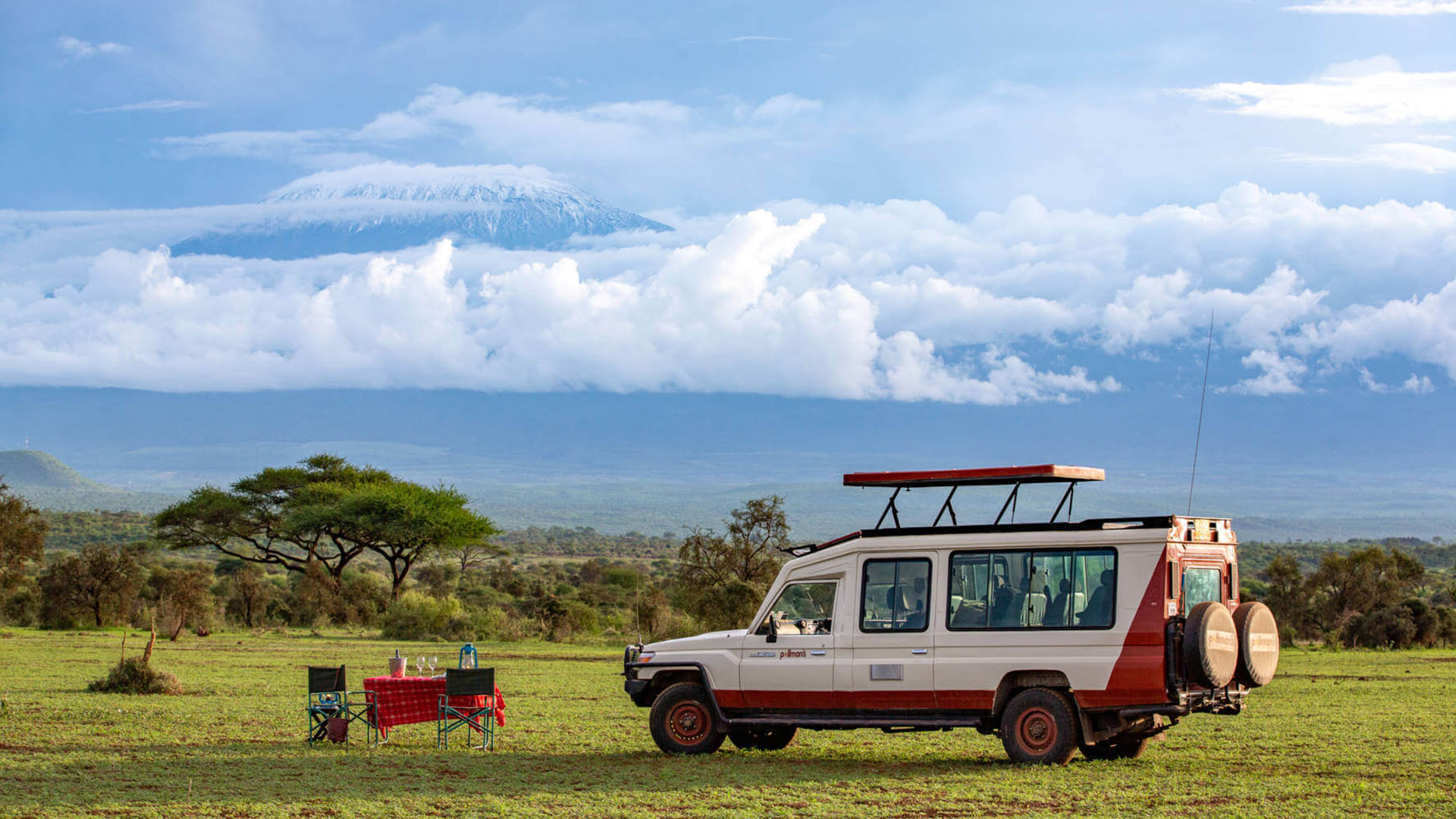Pollmans Safari Experience with Mount Kilimanjaro in View | Brimco Pollmans tours safari vehicle and dining setup in grassy plains with mount kilimanjaro and clouds in the background