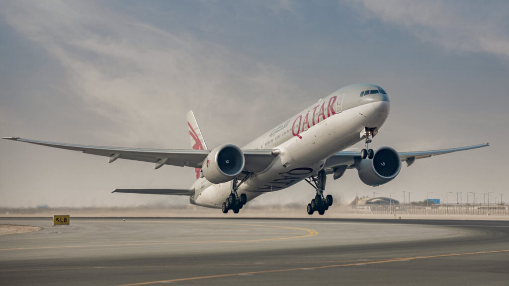 Qatar airways boeing 777 taking off from a runway with landing gear still extended