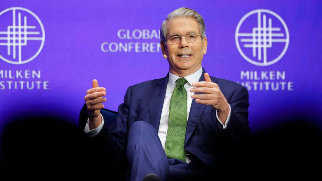 Scott bessent speaking on stage at the milken institute global conference with a purple background