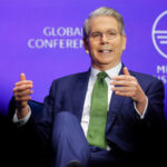 Scott bessent speaking on stage at the milken institute global conference with a purple background
