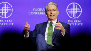 Scott bessent speaking on stage at the milken institute global conference with a purple background