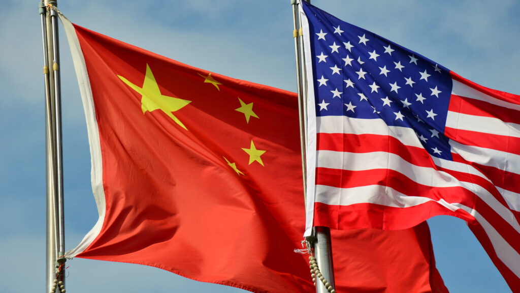 Close up image of the united states and china flags waving on flagpoles against a blue sky