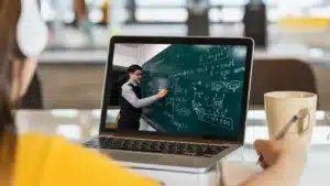 Student attending an online class on a laptop taking notes while learning complex math equations remotely