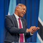 President duma boko speaking at a podium animatedly gesturing with hands with botswana flags in the background