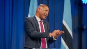 President duma boko speaking at a podium animatedly gesturing with hands with botswana flags in the background