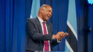 President duma boko speaking at a podium animatedly gesturing with hands with botswana flags in the background