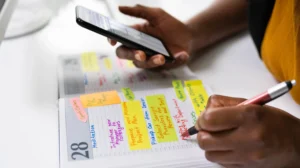 Person writing in a color coded planner while referencing a smartphone schedule